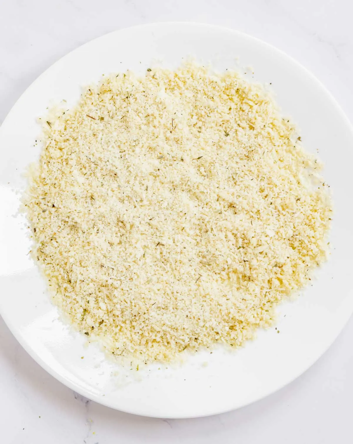 Plate with grated Parmesan, panko breadcrumbs, and herbs de Provence mixed together.