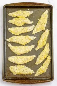 Perch fillets coated in Parmesan and Panko breading arranged on a baking sheet and sprayed with oil.