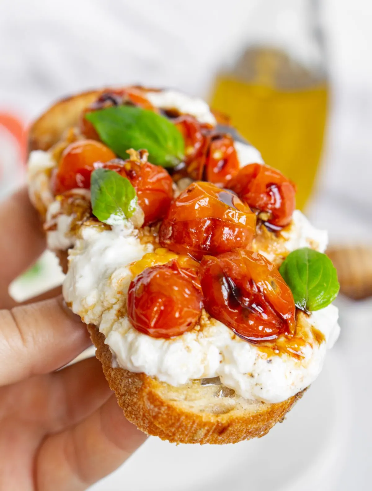 Hand holding burrata toast with blistered tomatoes and crispy garlic