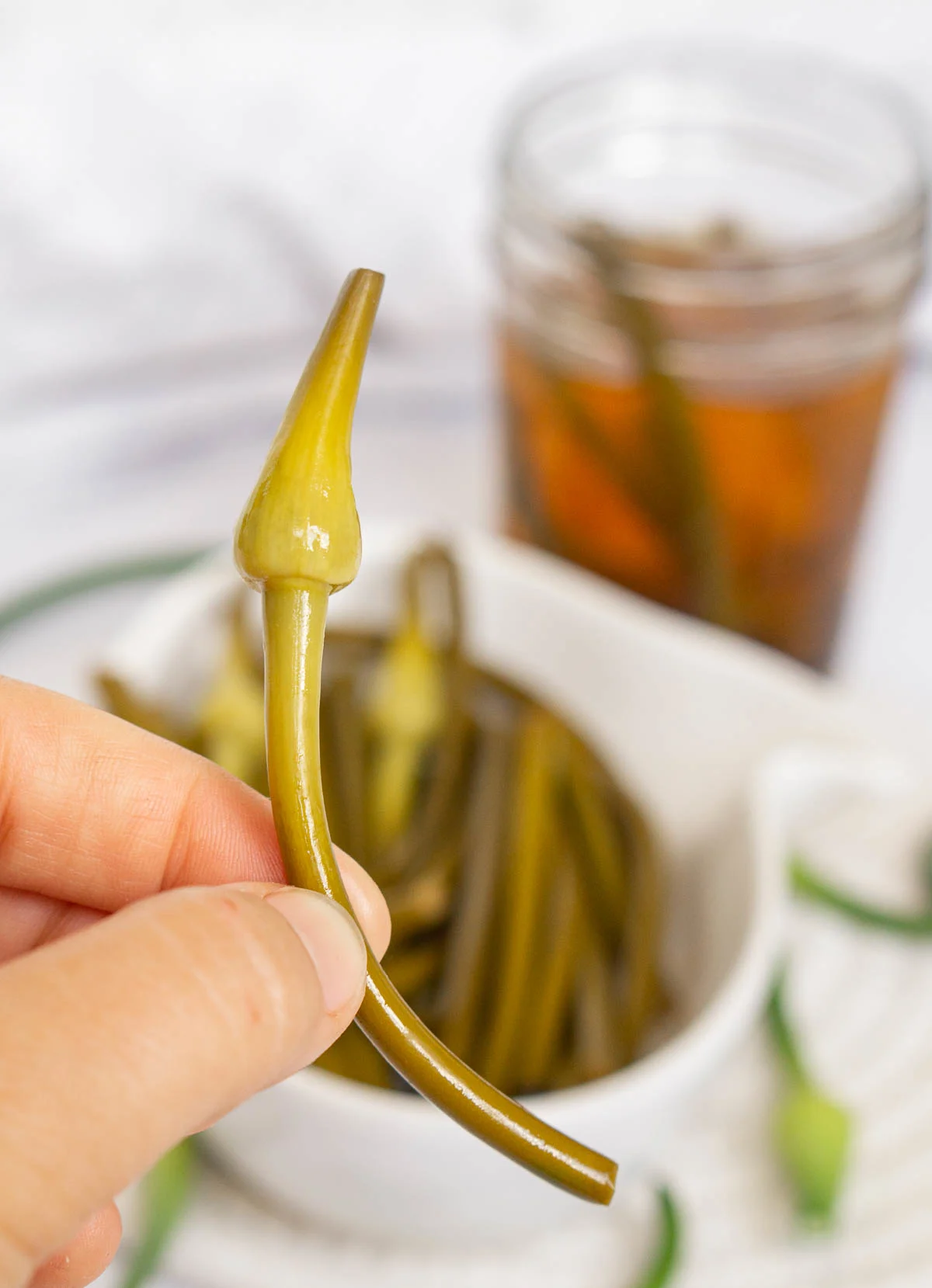 Hand holding a pickled garlic scape