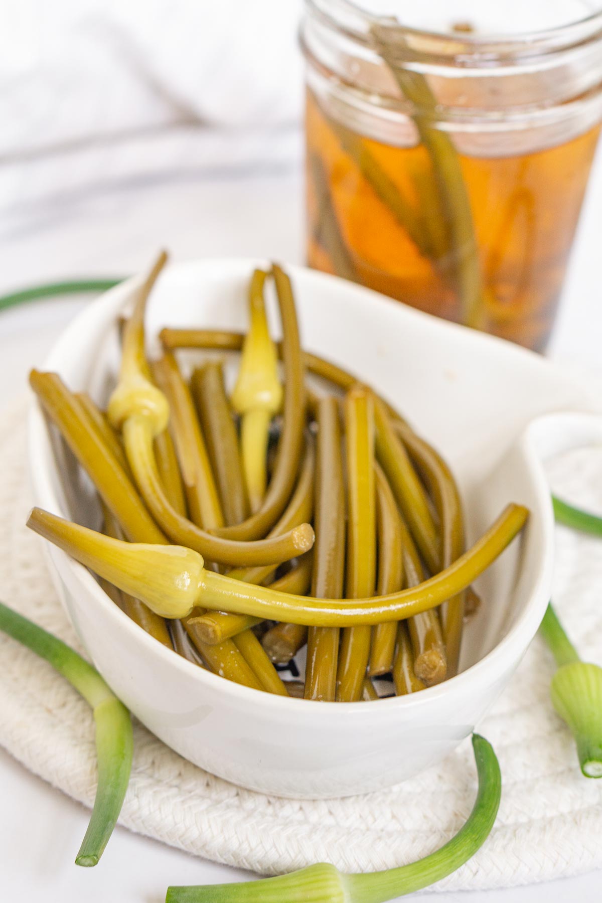 Plate of pickled garlic scapes with a jar in the background