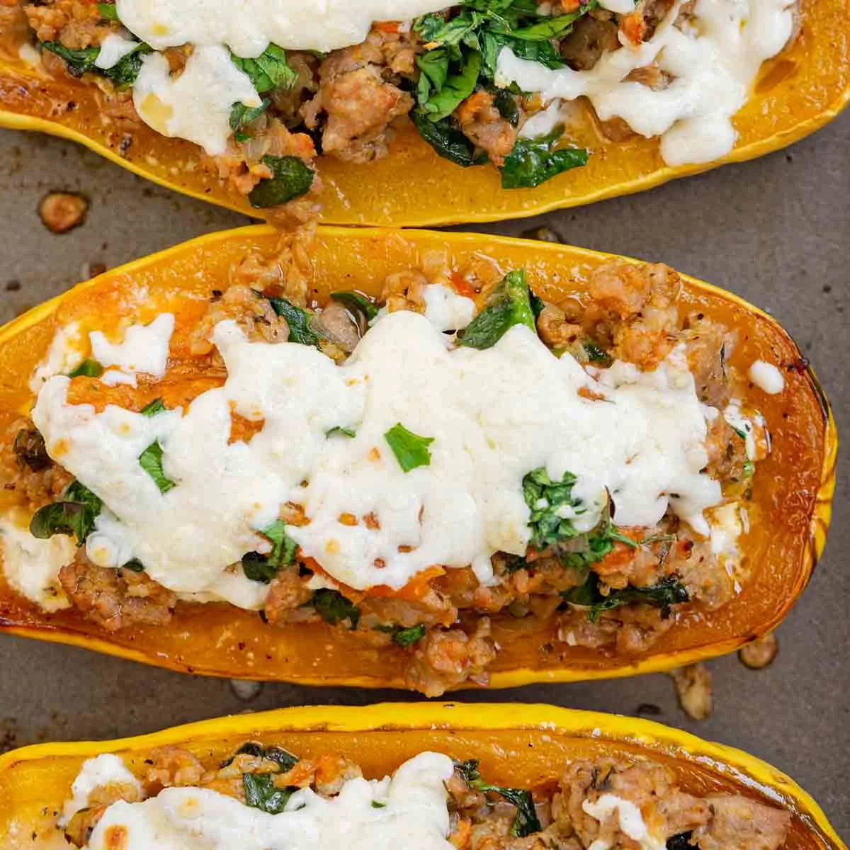 Sausage stuffed delicata squash with melted cheese on top.