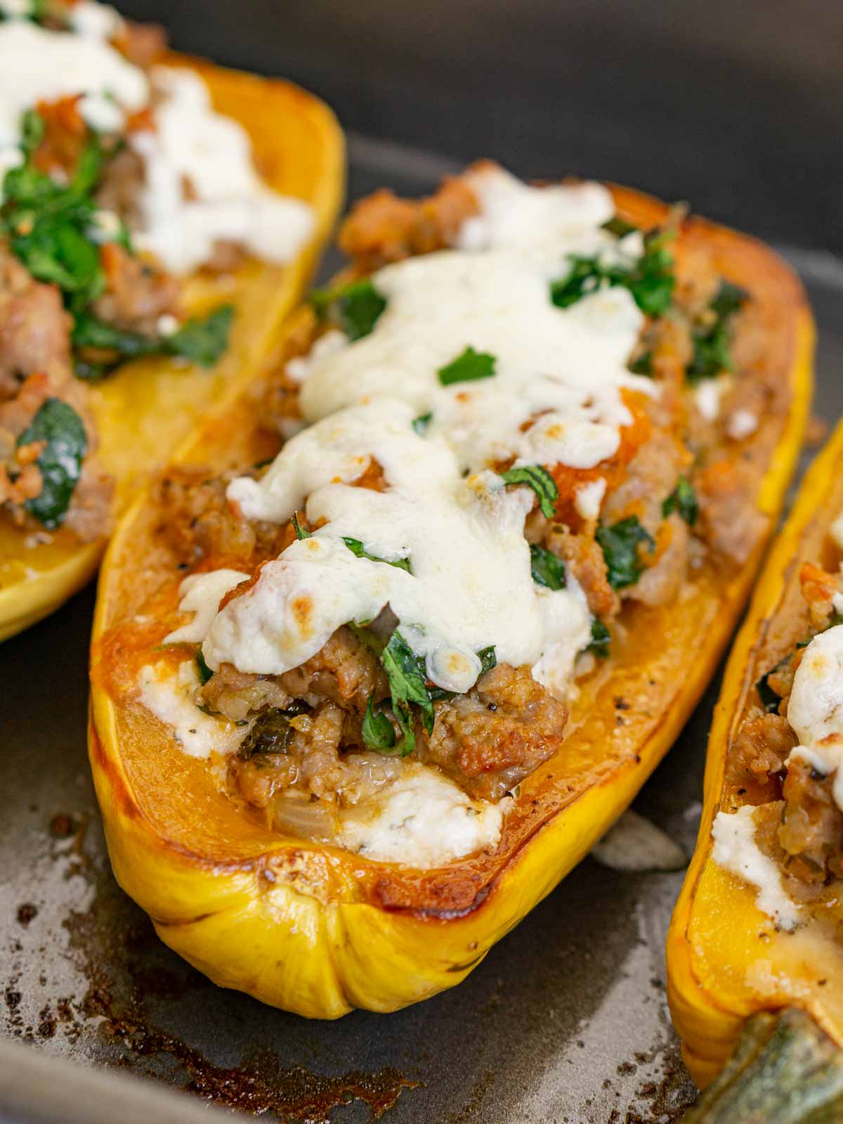Close up of a stuffed delicata squash with Italian sausage and mozzarella on top to show texture.
