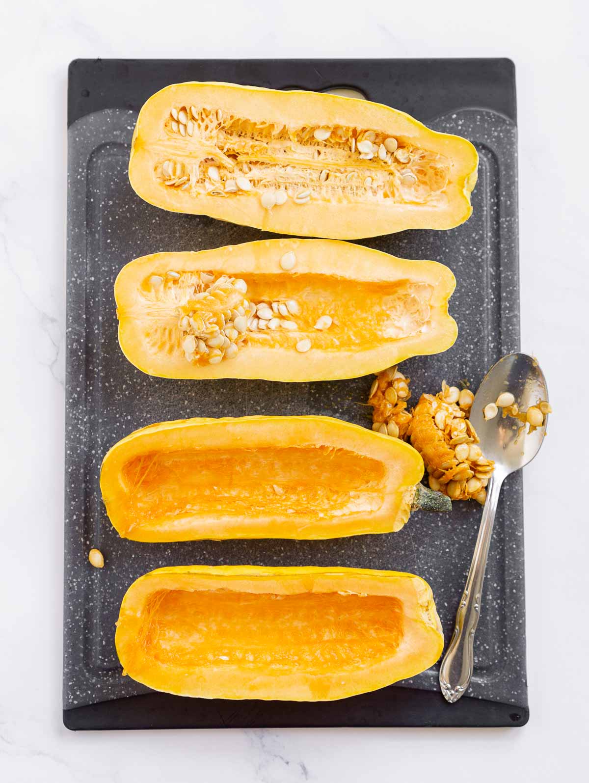 Delicata squash halves with seeds being removed with a spoon