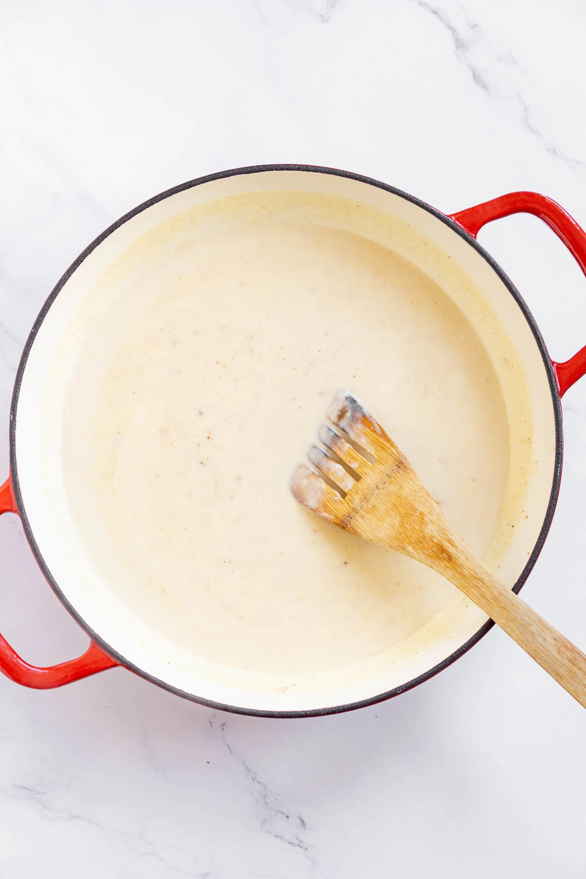 Chicken broth and cream added to roux in a pan to make a creamy chicken gravy