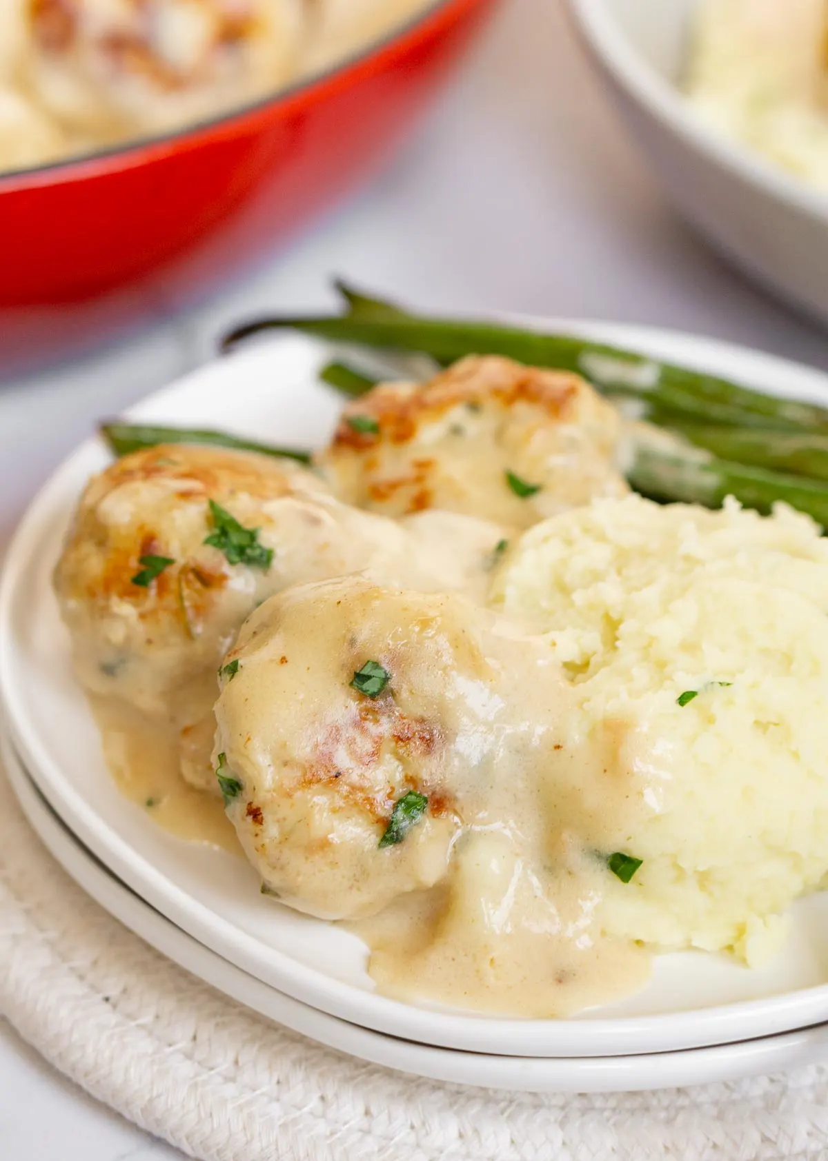 Swedish chicken meatballs covered in creamy gravy on a plate with mashed potatoes and green beans