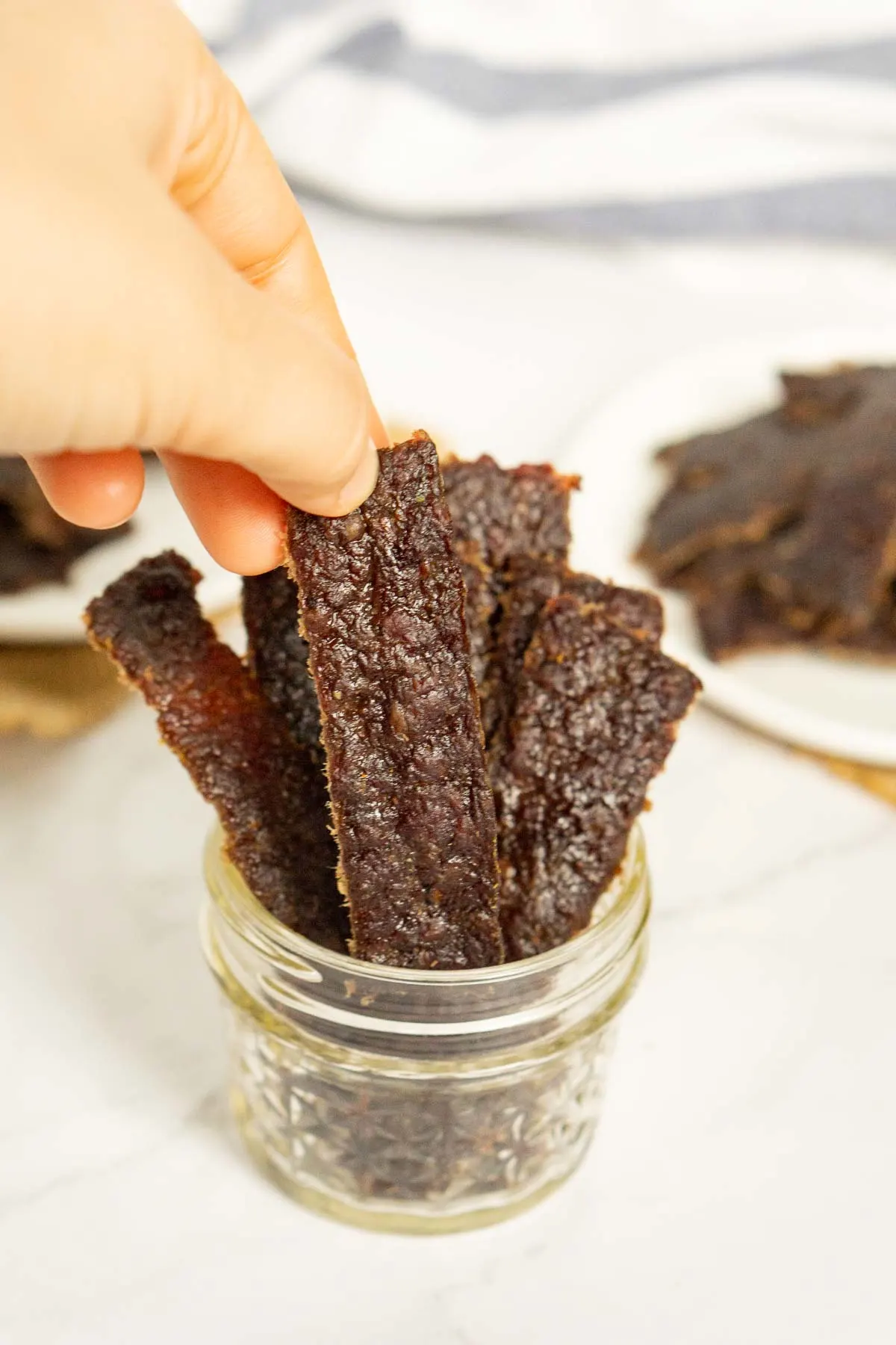 Hand grabbing a piece of sweet and spicy ground jerky