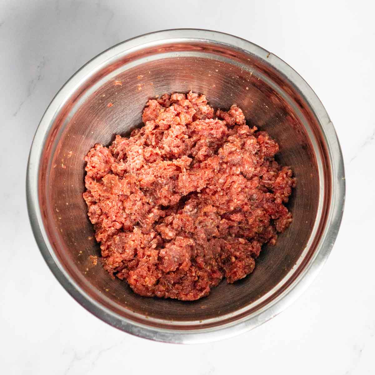 Ground beef mixed with seasonings in a bowl