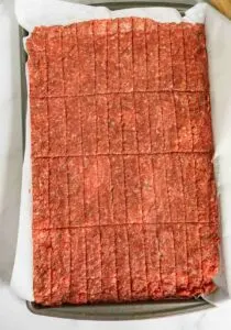 Ground beef mixture pressed into a baking sheet and cut into rectangles to make it easy to tear into jerky after dehydrating