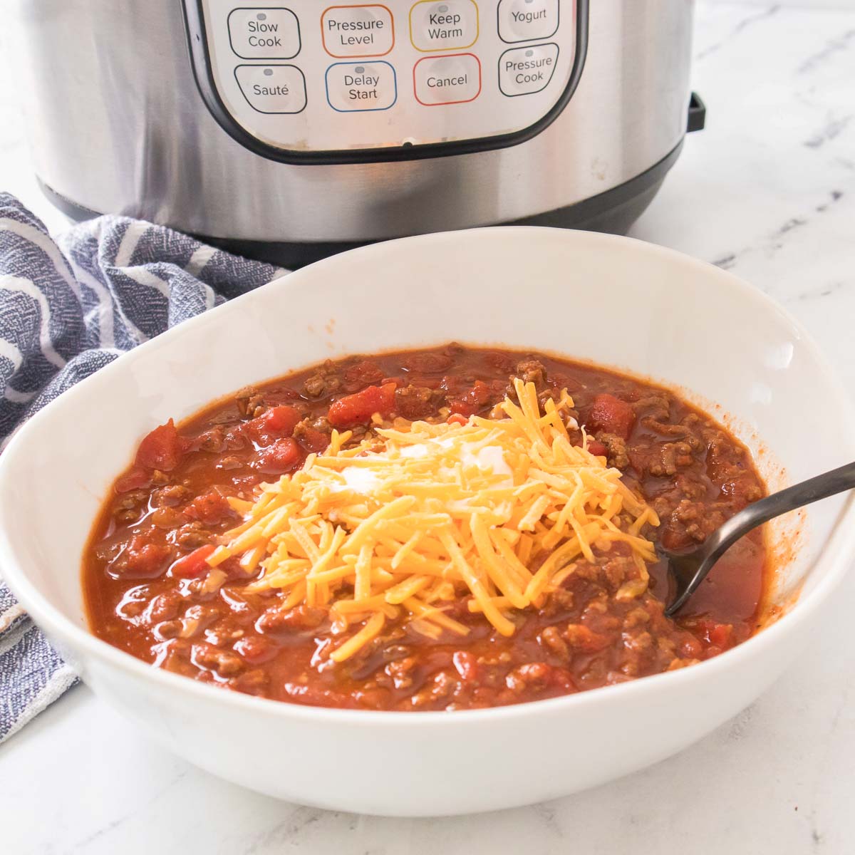 Bowl of chili without beans topped with sour cream and shredded cheese.