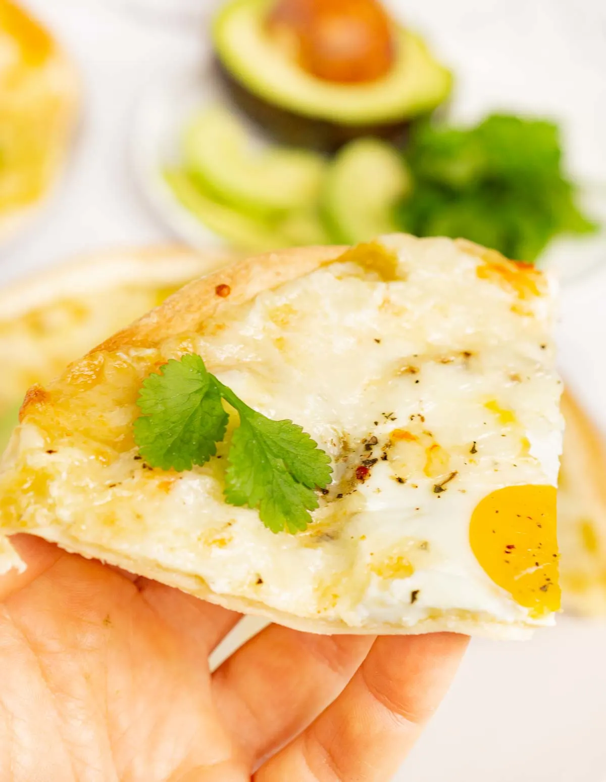 Hand holding slice of Mexican-style tortilla breakfast pizza