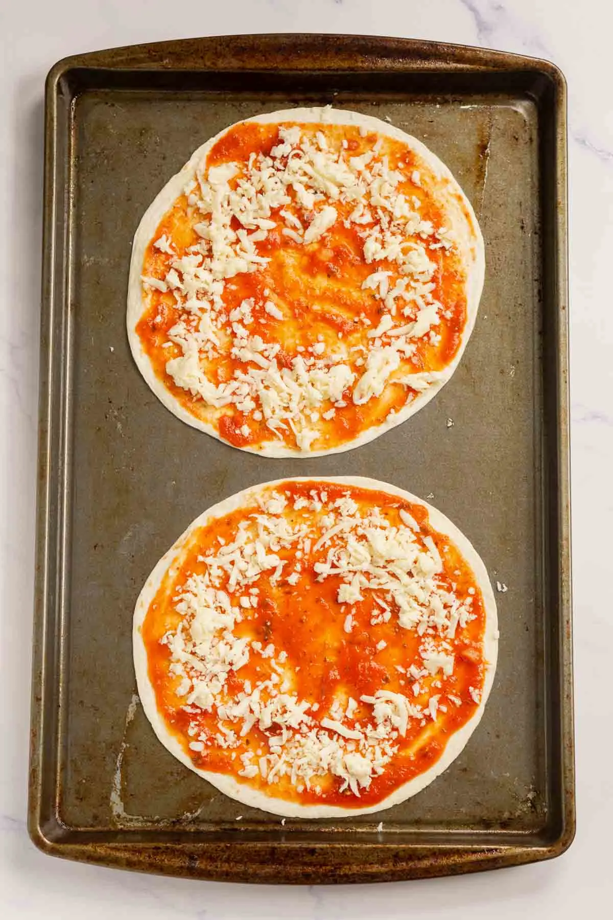 Shredded cheese sprinkled on a tortilla with pizza sauce