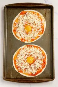 Assembled breakfast pizzas on a tortilla on a baking sheet