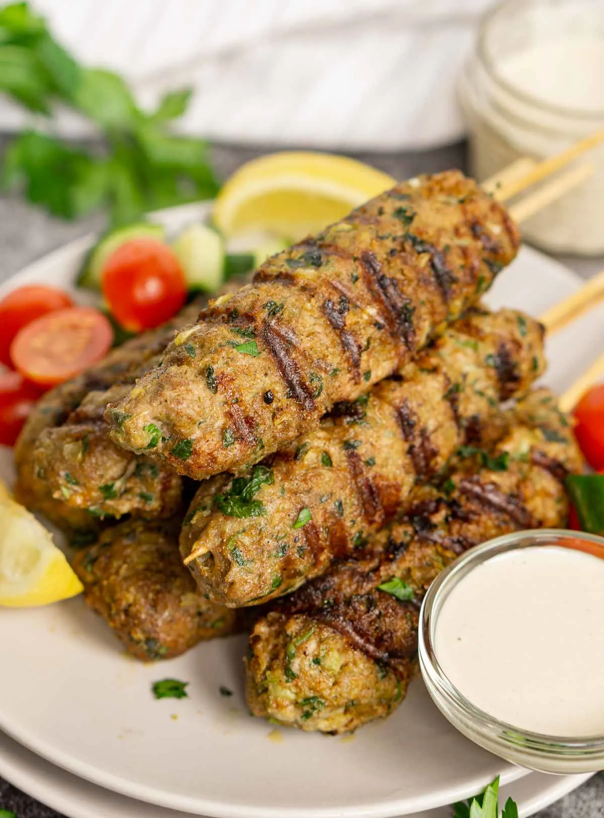 Plate of pork kofta skewers with dip and garnishes on the side.