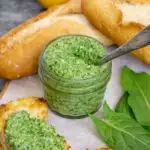 Jar of sour leaf sorrel pesto with baguettes and garnishes around it