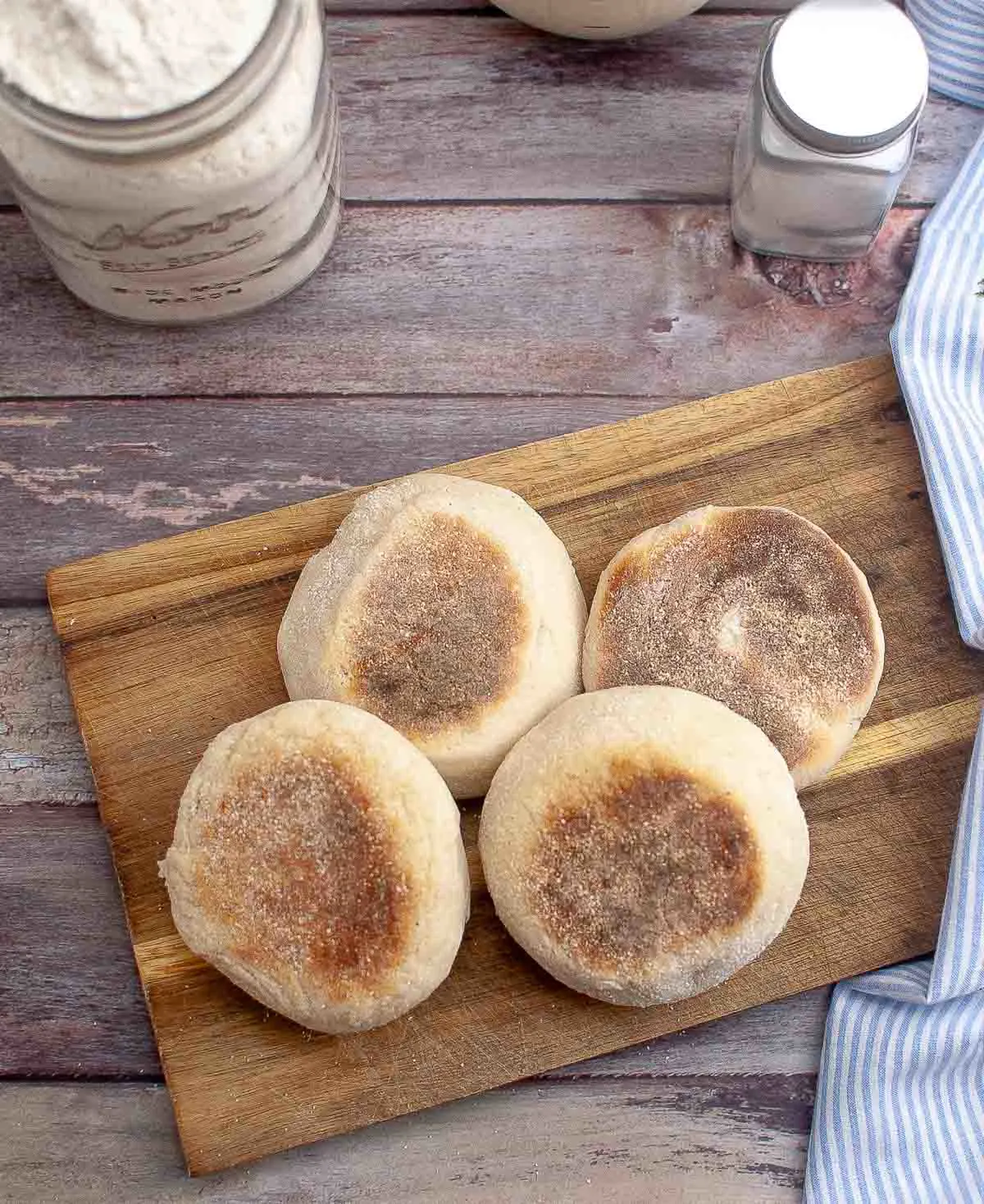 Sourdough English muffins on a cutting board with sourdough starter jar in the background