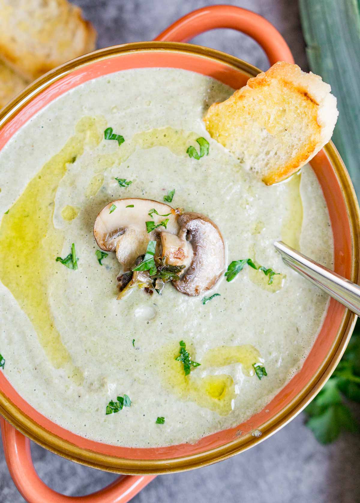 Close up of a bowl of creamy mushroom leek soup with a slice of toasted baguette