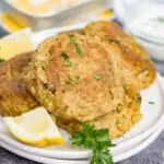 Sardine cakes on a plate with lemon wedges