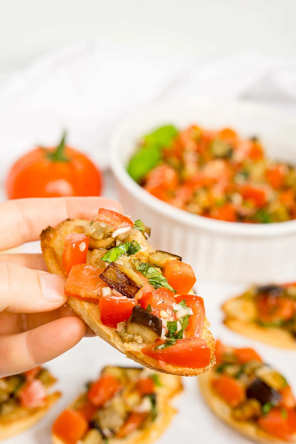 Hand holding a piece of eggplant bruschetta crostini appetizer