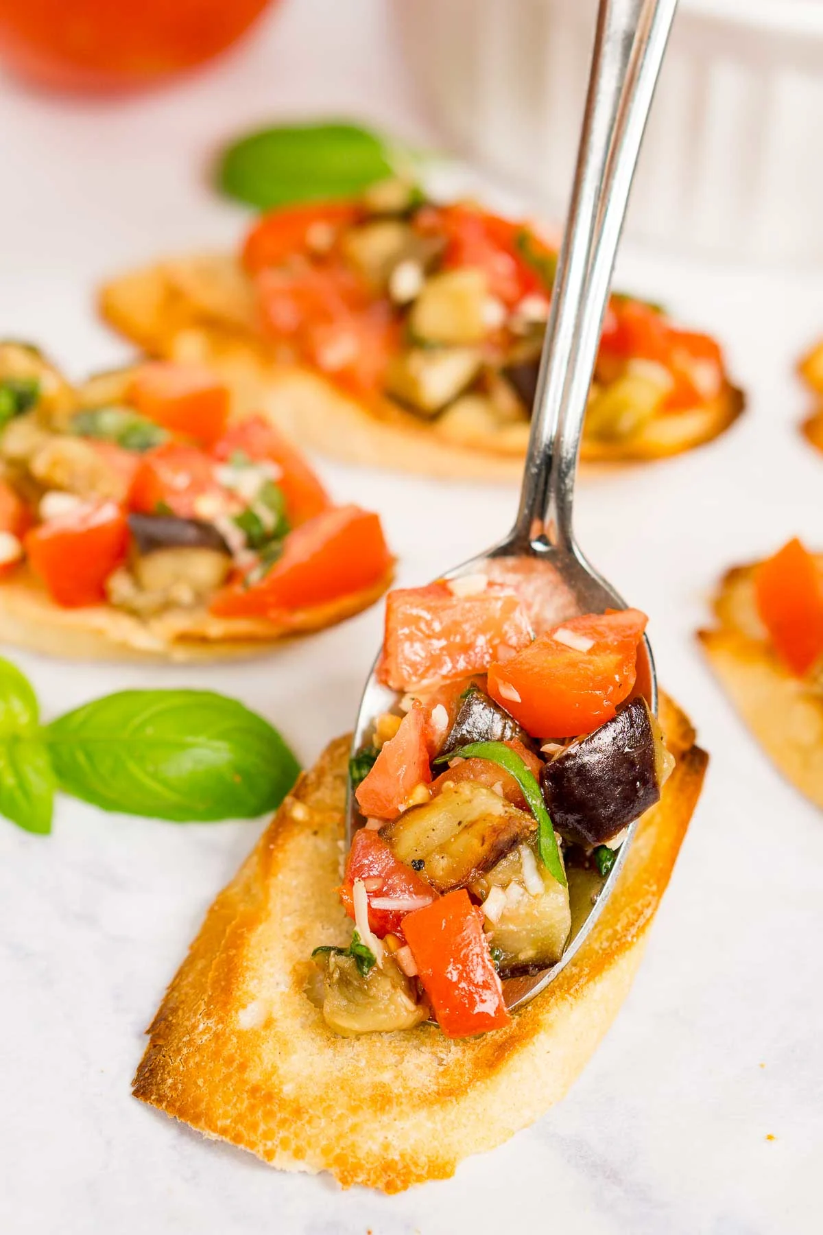 Spooning roasted eggplant and tomato bruschetta onto a sliced baguette