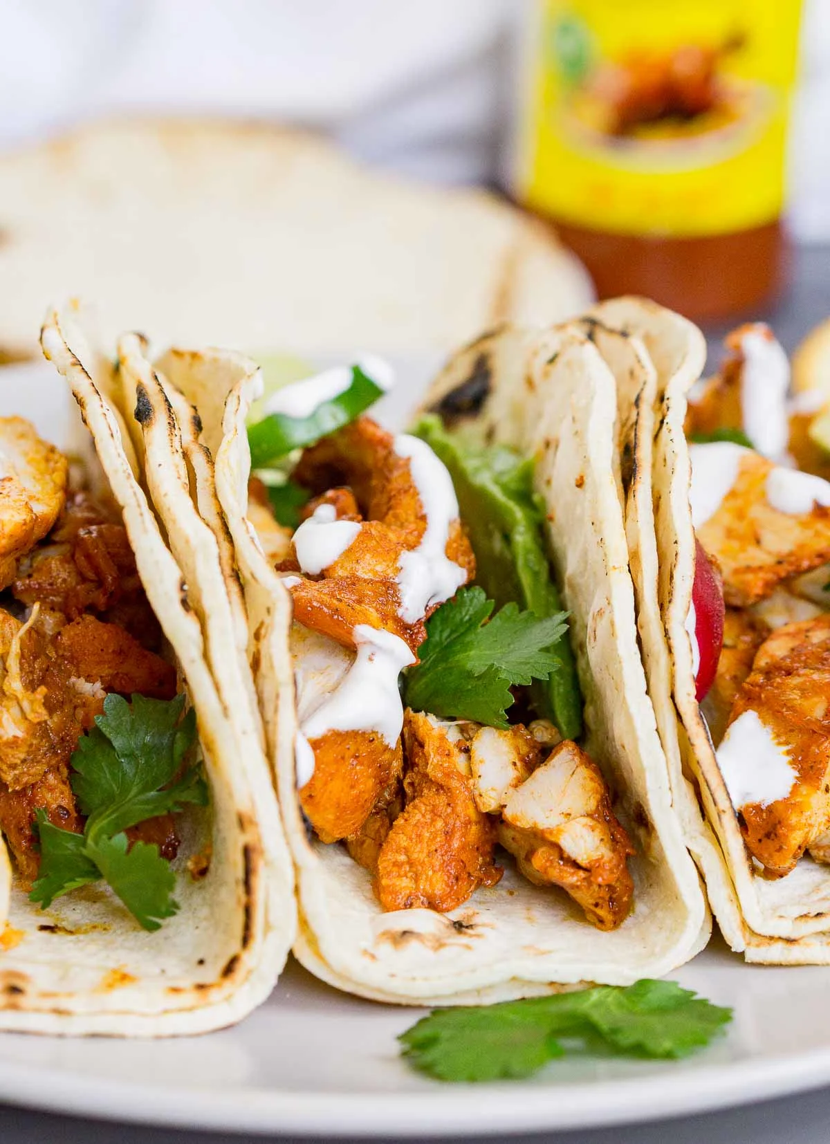 3 achiote chicken tacos on a plate with cilantro and sour cream garnish