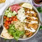 Harissa chicken bowls over couscous with veggies, pickled onions, garlic sauce, and naan
