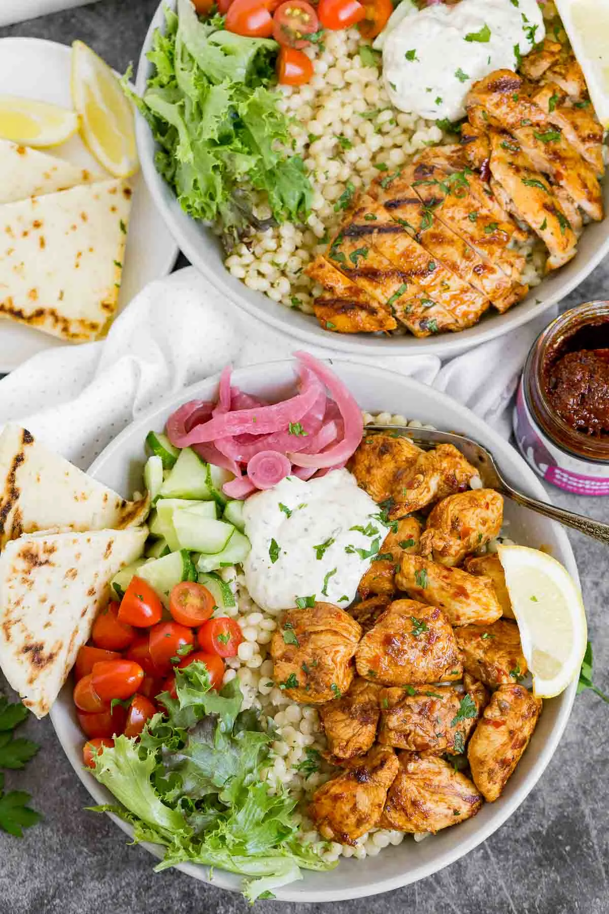 Harissa chicken bites over couscous with veggies, pickled onions, garlic sauce, and naan