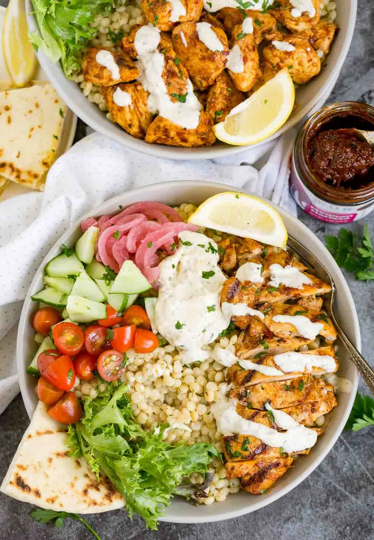 Couscous harissa chicken bowls with veggies, pickled onions, and garlic sauce