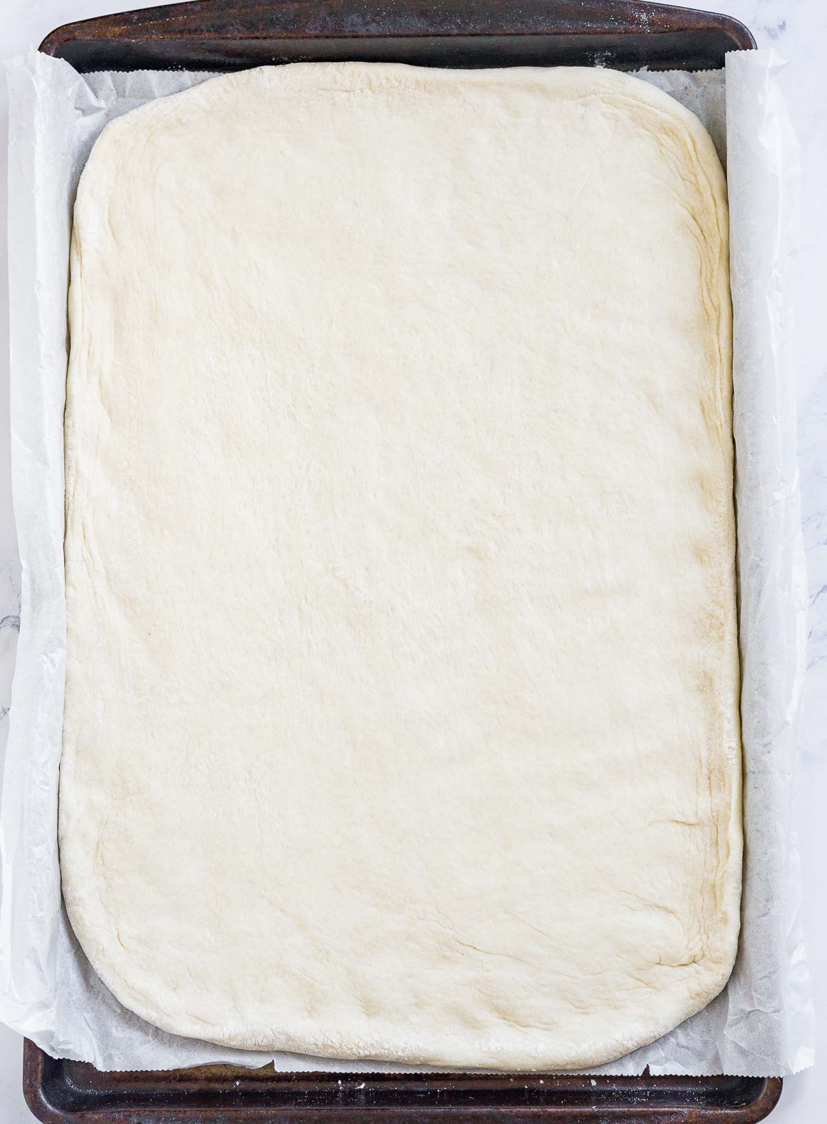 Pizza dough stretched out on a baking sheet lined with parchment paper