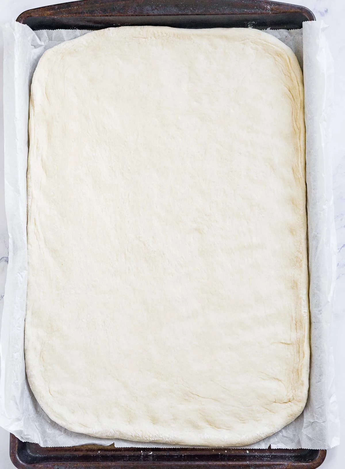 Pizza dough stretched out on a baking sheet lined with parchment paper