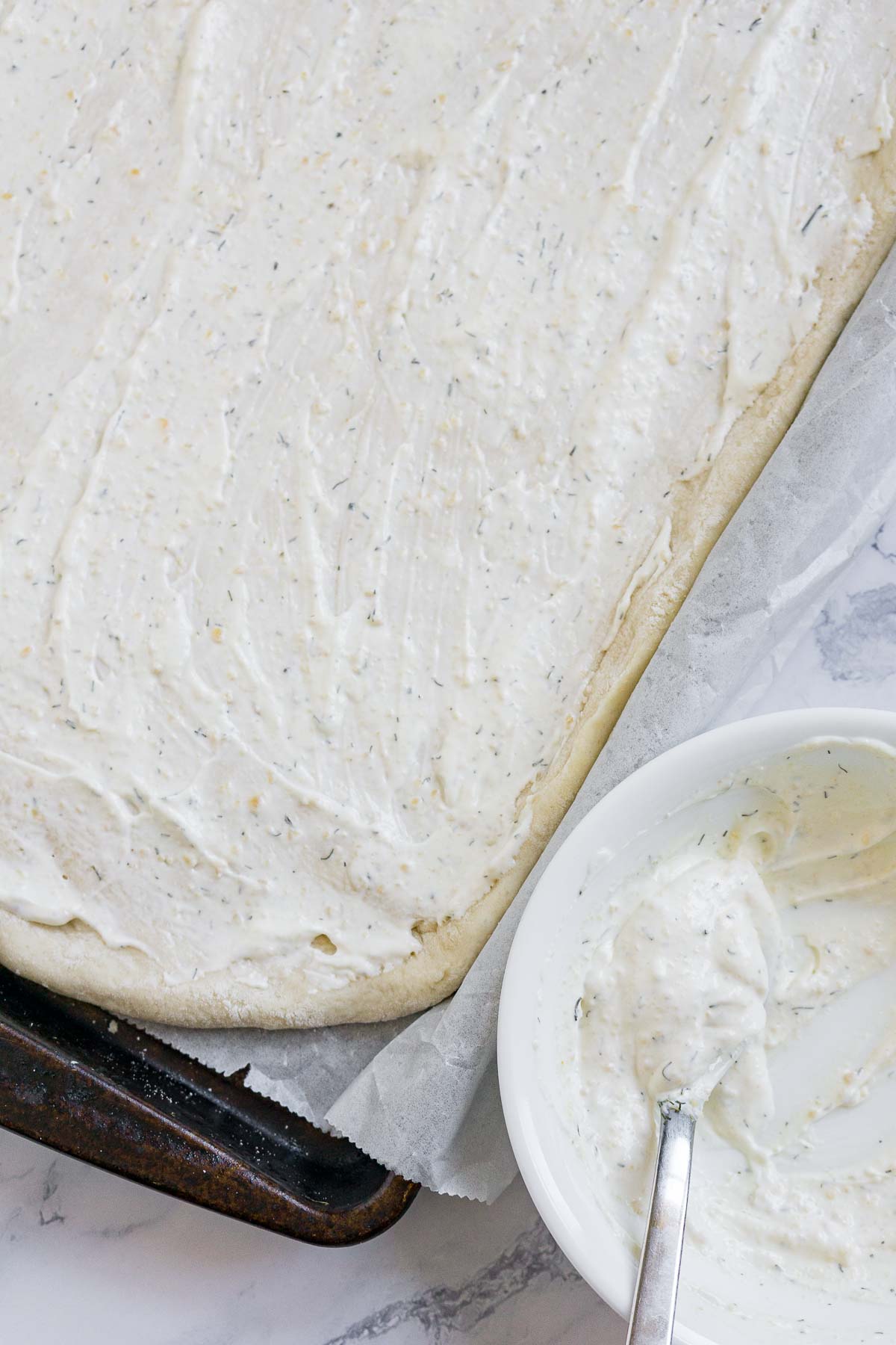 Spreading white pizza sauce on pizza dough