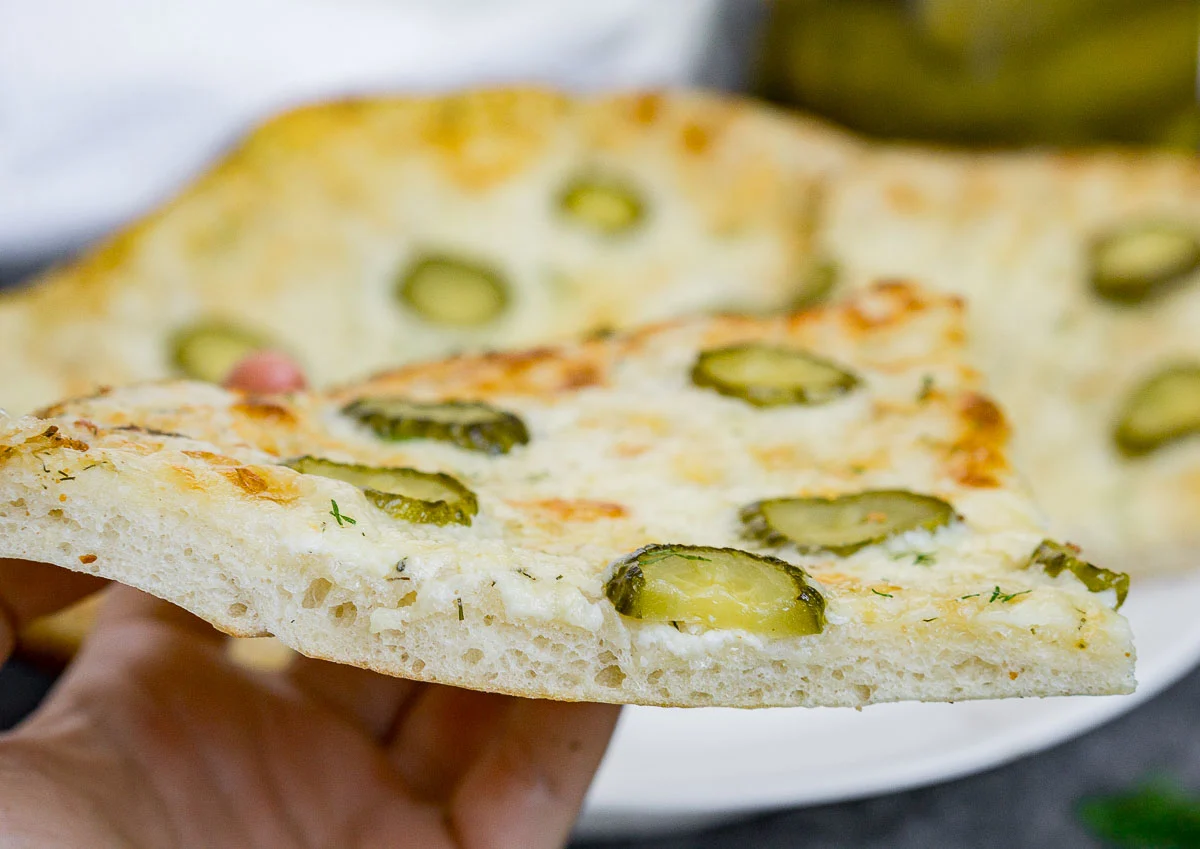 Hand holding slice of dill pickle pizza to show texture