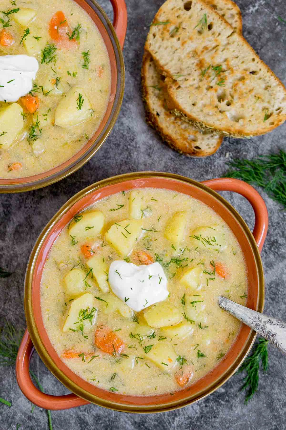 Two bowls of potato dill soup garnished with sour cream and dill