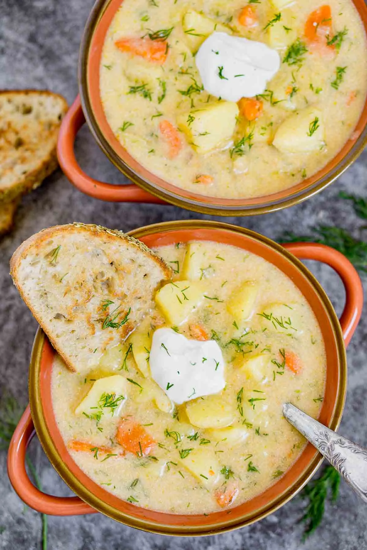 Bowls of potato dill soup topped with sour cream, dill, and a slice of crusty bread