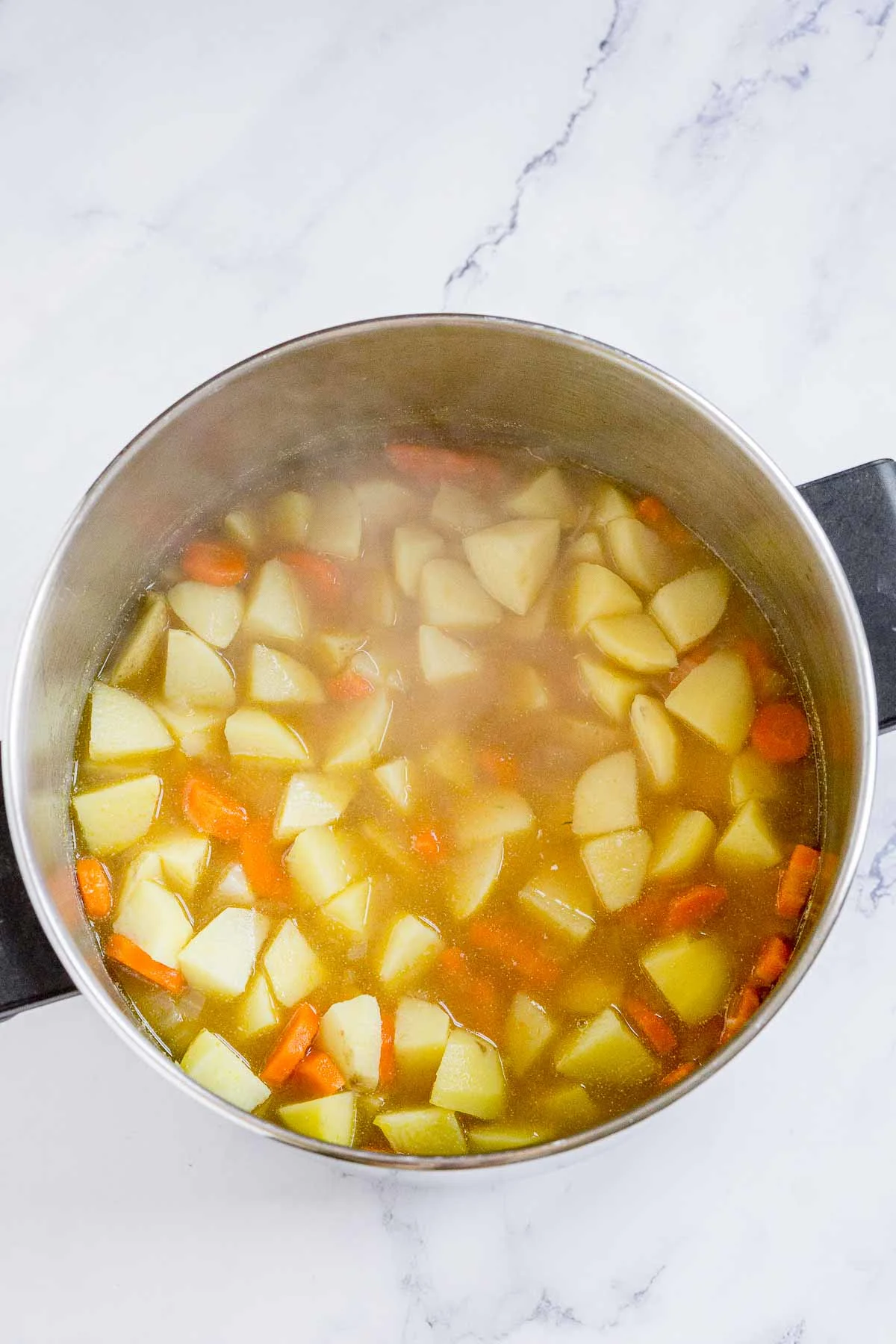 Cooked potatoes and carrots in a soup pot